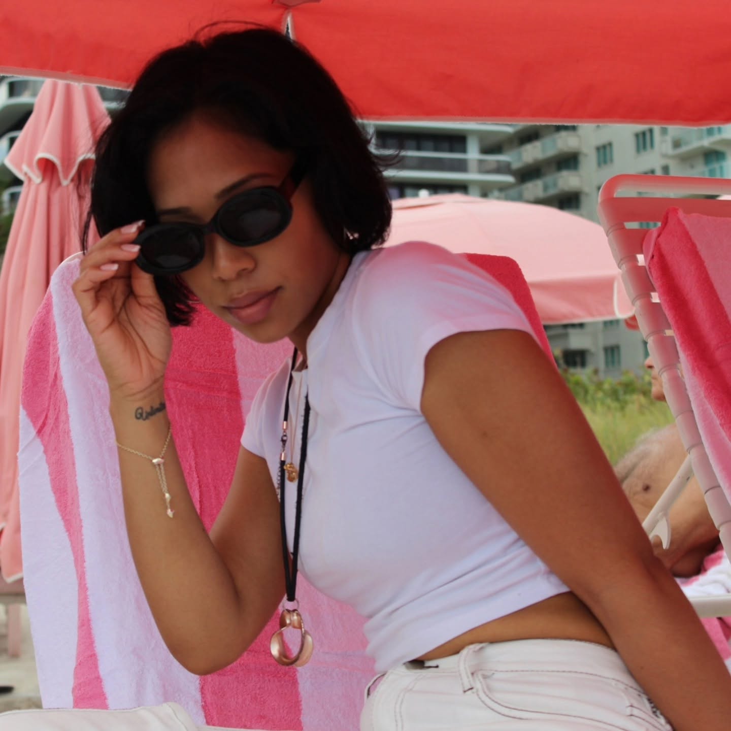 Dorothy Tobias-Williams adjusting black sunglasses while relaxing in a white top on a pink poolside lounge chair.